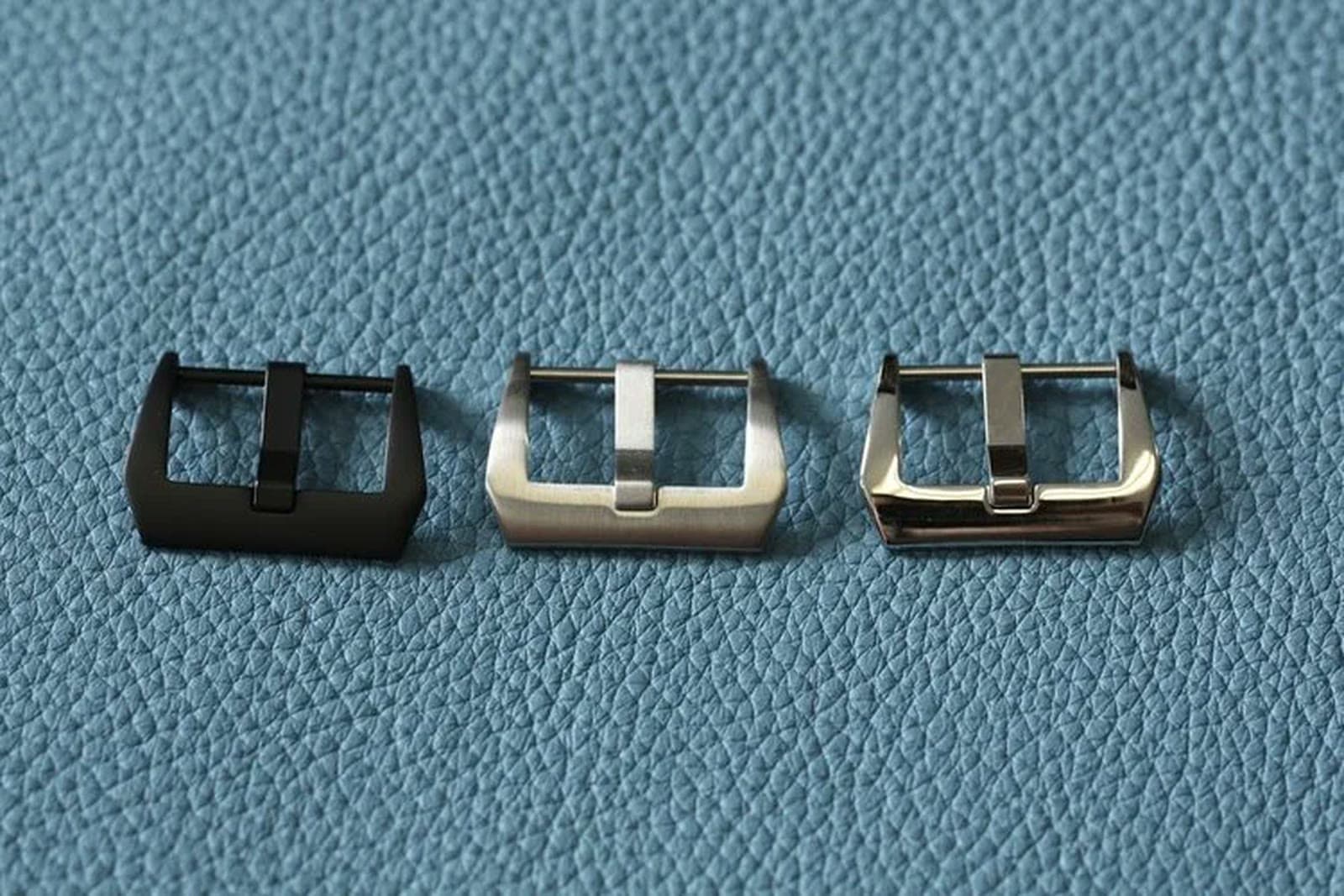 Three pin buckles — black, brushed, and polished steel — on leather.